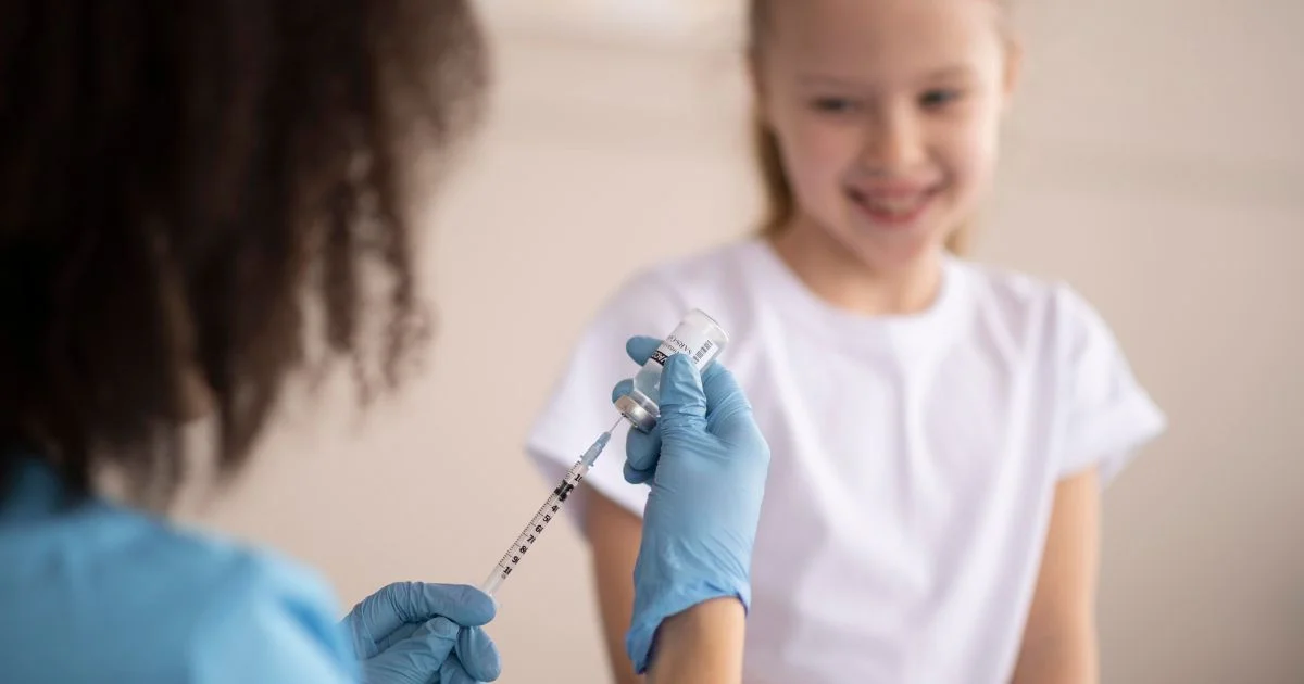 Nurse preparing vaccine syringe while child smiles